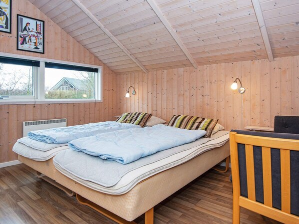 A wooden-paneled room with two beds, a window, and a desk.