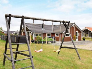 Un ensemble de balançoires en bois installé dans un espace herbeux, avec un immeuble d’habitation en arrière-plan.
