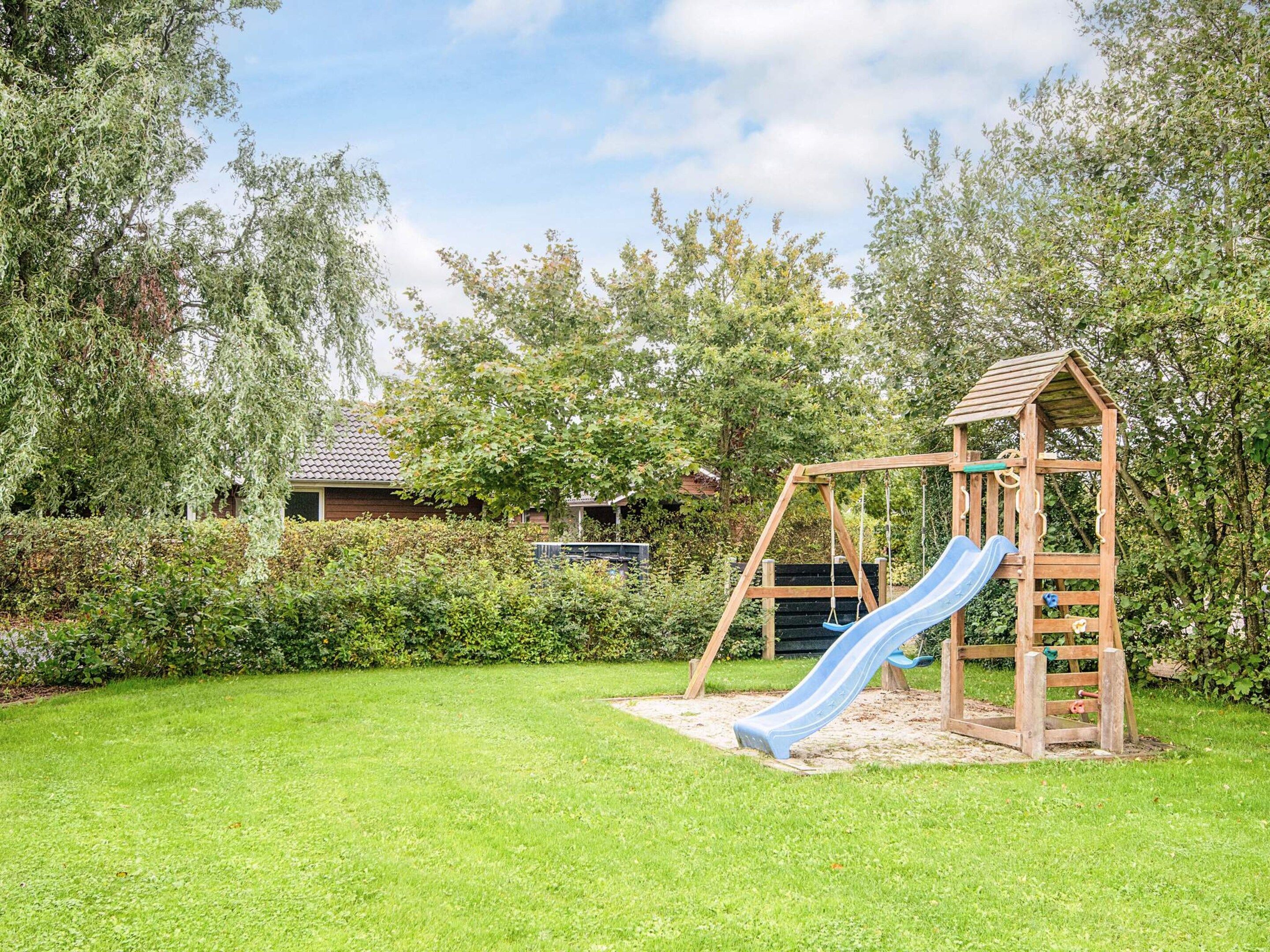 A wooden play structure with a slide in a grassy backyard.