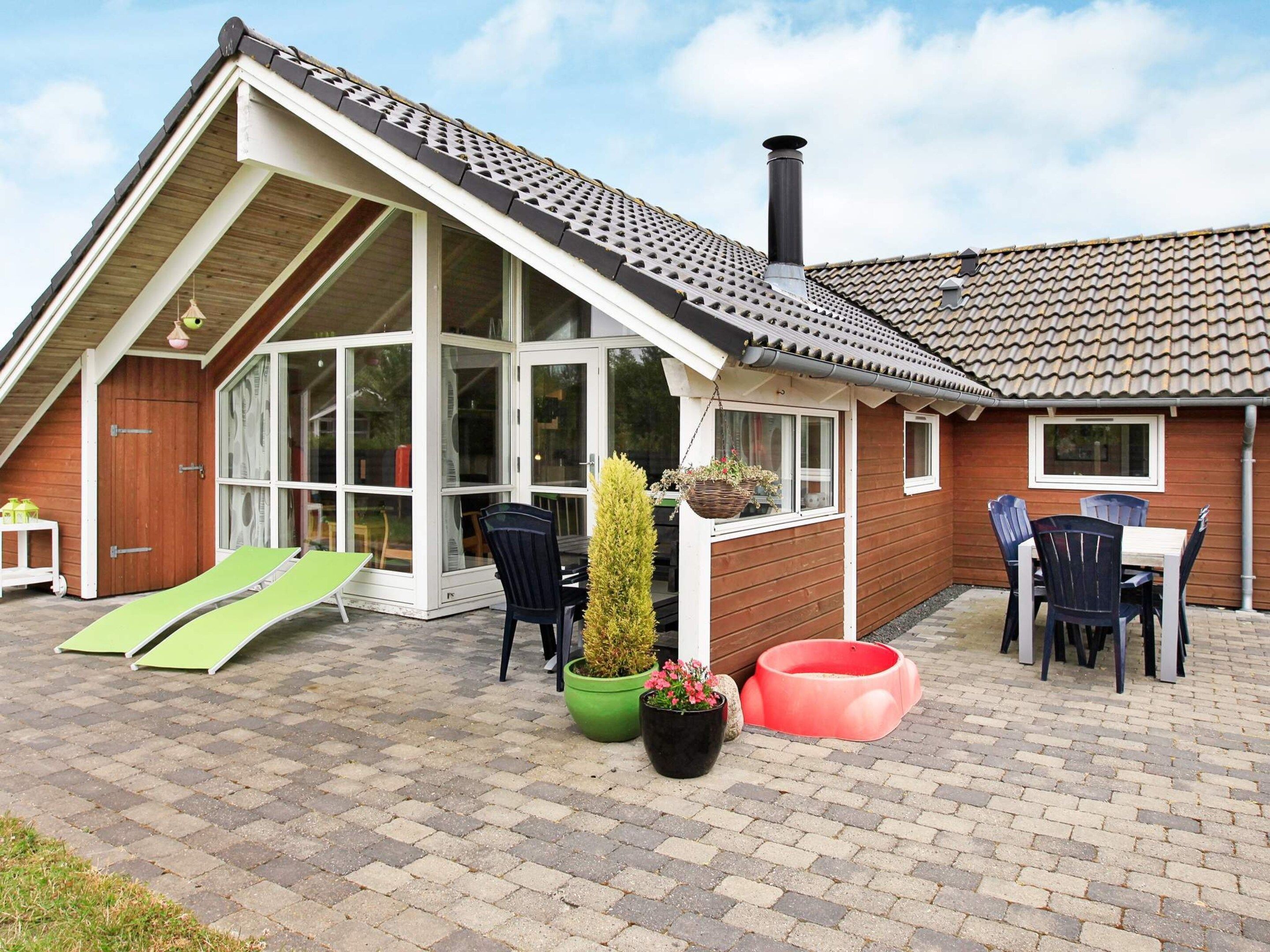 A house with a sloped roof, large windows, and a patio area with outdoor furniture.