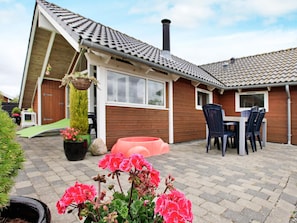 A residential building with a sloped roof, a chimney, and a patio area with a table and chairs.