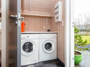 A compact laundry room with two front-loading washing machines, a small shelf, and a power outlet.