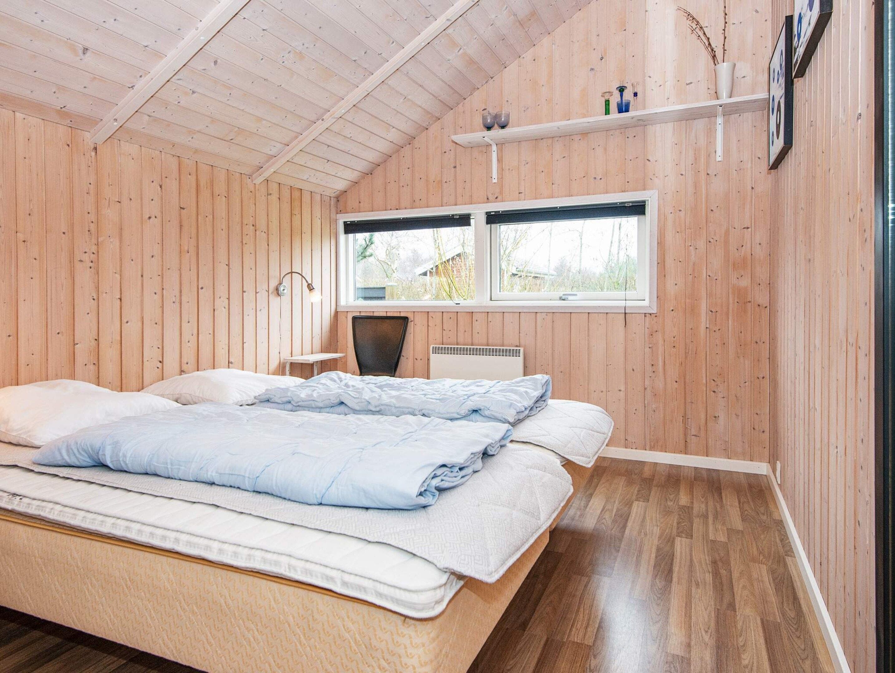 A bedroom with a bed, a chair, a desk, a window, and a shelf with items.