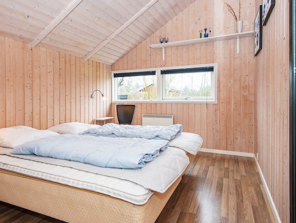 A bedroom with a bed, a chair, a desk, a window, and a shelf with items.