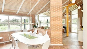 Une pièce spacieuse avec une grande table blanche, des chaises blanches et un pilier en briques.