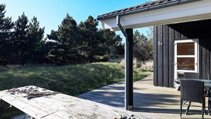 Une terrasse en bois avec une table et des chaises, une colonne en métal noir et un bâtiment doté d’une fenêtre et d’une porte portant l’inscription « 5A ».
