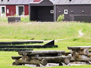 A rustic outdoor setting with wooden benches and a path leading to a red and black building.