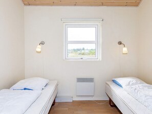 A room with two beds, a window, and a wall-mounted heater.