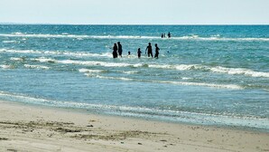 A beach with people walking in the water and on the shore.