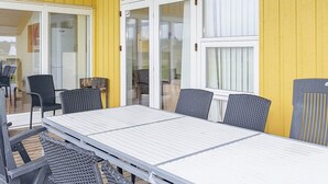 A covered outdoor seating area with a table and chairs, large windows, and a yellow wall.