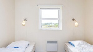 A small, single-room accommodation with two beds, a window, and a wall-mounted heater.