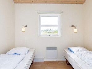 A small, single-room accommodation with two beds, a window, and a wall-mounted heater.