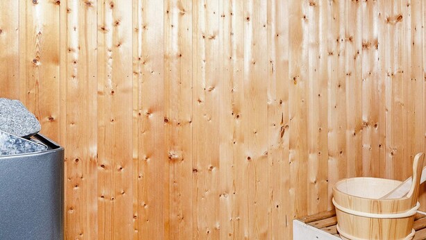 A sauna room with a wooden wall, a stone container, and a wooden basin with a ladle.