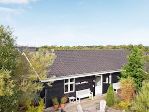 A black villa with the name "VILLA VANILLA" on the facade, a wooden deck with two white chairs, and a bench outside.