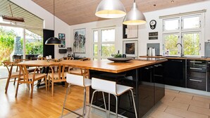 Eine moderne Küche mit einem Holztisch, Barhocker, Pendelleuchten und Blick ins Freie.
