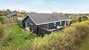 Ein modernes Haus mit dunkler Fassade, geneigtem Dach und einer kleinen Terrasse.