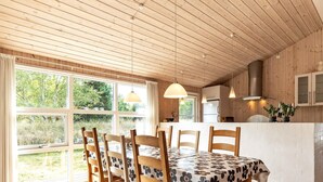 A wooden interior with a dining table, chairs, a kitchen area, and large windows. - 4 Star Holiday Home in Albaek (Aalbaek)