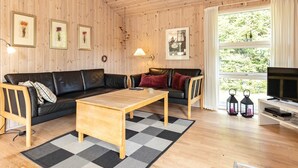 A cozy living room with a wooden ceiling, a black leather sofa, a wooden coffee table, and a television on a white stand. - 4 Star Holiday Home in Albaek (Aalbaek)