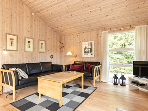 A cozy living room with a wooden ceiling, a black leather sofa, a wooden coffee table, and a television on a white stand. - 4 Star Holiday Home in Albaek (Aalbaek)
