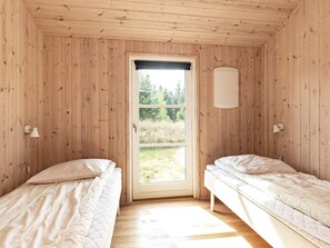 A room with two beds, a window, and a wall-mounted light fixture.