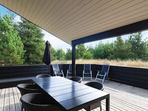 A covered outdoor seating area with a table and chairs, surrounded by a wooden deck and a view of trees. - 4 Star Holiday Home in Albaek (Aalbaek)