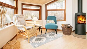 Une pièce chaleureuse avec un plafond en bois, un poêle à bois noir, des meubles en osier et de grandes fenêtres.