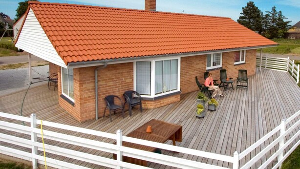A two-story house with a red-tiled roof, a deck with outdoor furniture, and a white fence. - 4 Star Holiday Home in Humble (Sydlangeland)