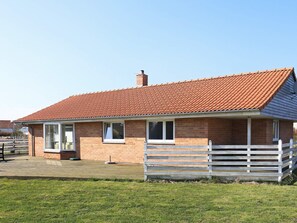 Een huis met één verdieping, gebouwd van baksteen, met een dak van rode tegels, een voortuin met een witte hek en een verharde oprit.