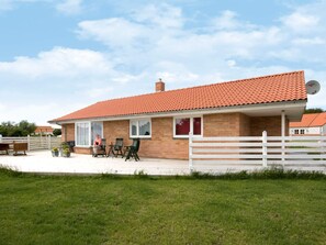 Een gelijkvloers huis van baksteen met een rode dakbedekking, een witte hekken en een terras met tuinmeubilair.