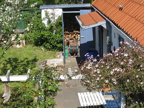Une propriété résidentielle avec un abri de jardin bleu, un banc en bois et un jardin agrémenté de plantes en fleurs.