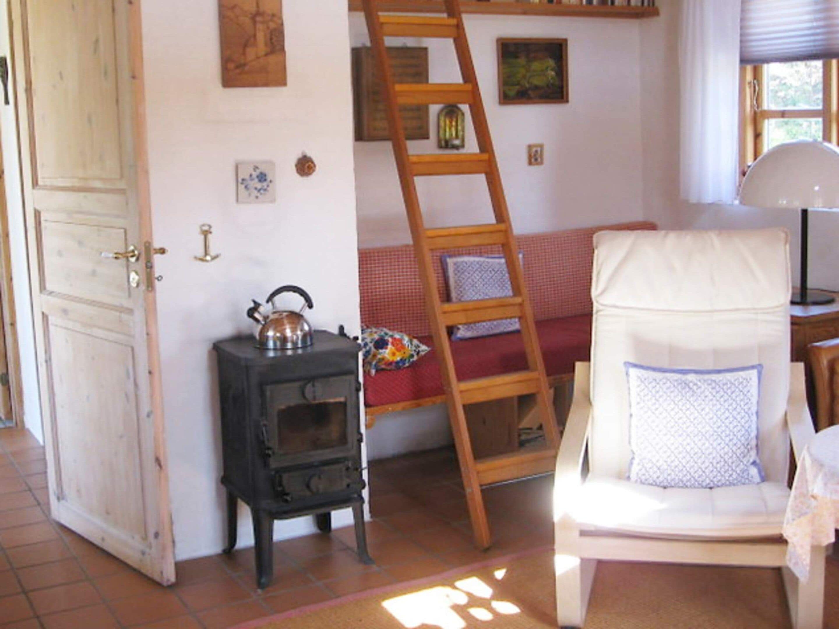 Een kamer met een houten deur, een klein fornuis, een ladder, een bank en een stoel met kussen.