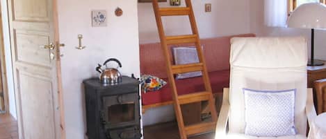 A room with a wooden door, a small stove, a ladder, a sofa, and a chair with a cushion.