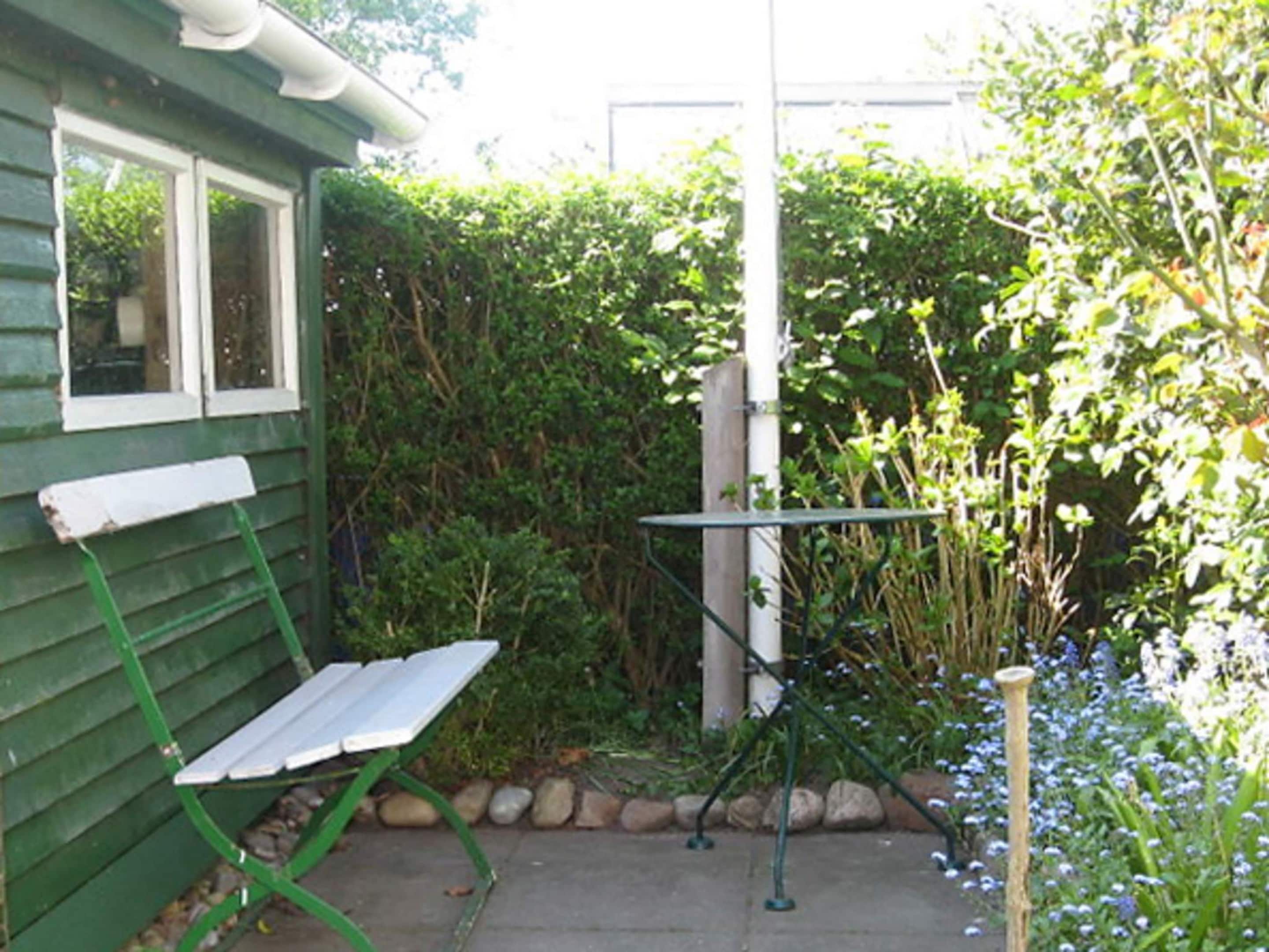 A green house with a bench and a table outside.
