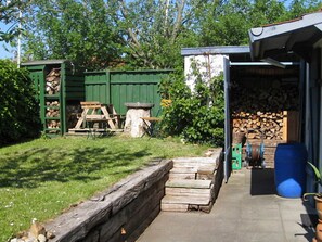 A wooden deck with a stone wall, a green shed with a ladder, and a stack of firewood. - 4 Star Holiday Home in Bramming (Bramming)
