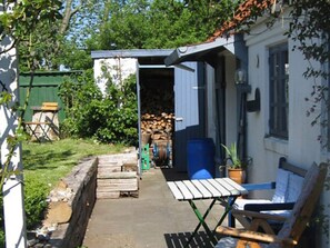 A small outdoor area with a wooden bench, a table, and a shed with a stack of firewood. - 4 Star Holiday Home in Bramming (Bramming)