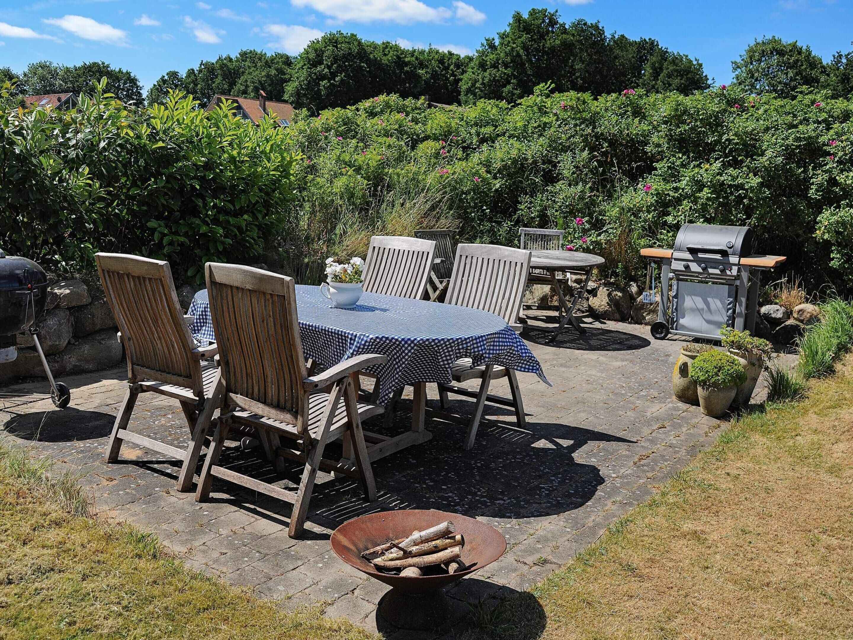 An outdoor patio with a table and chairs, a grill, and a wheelbarrow with logs.