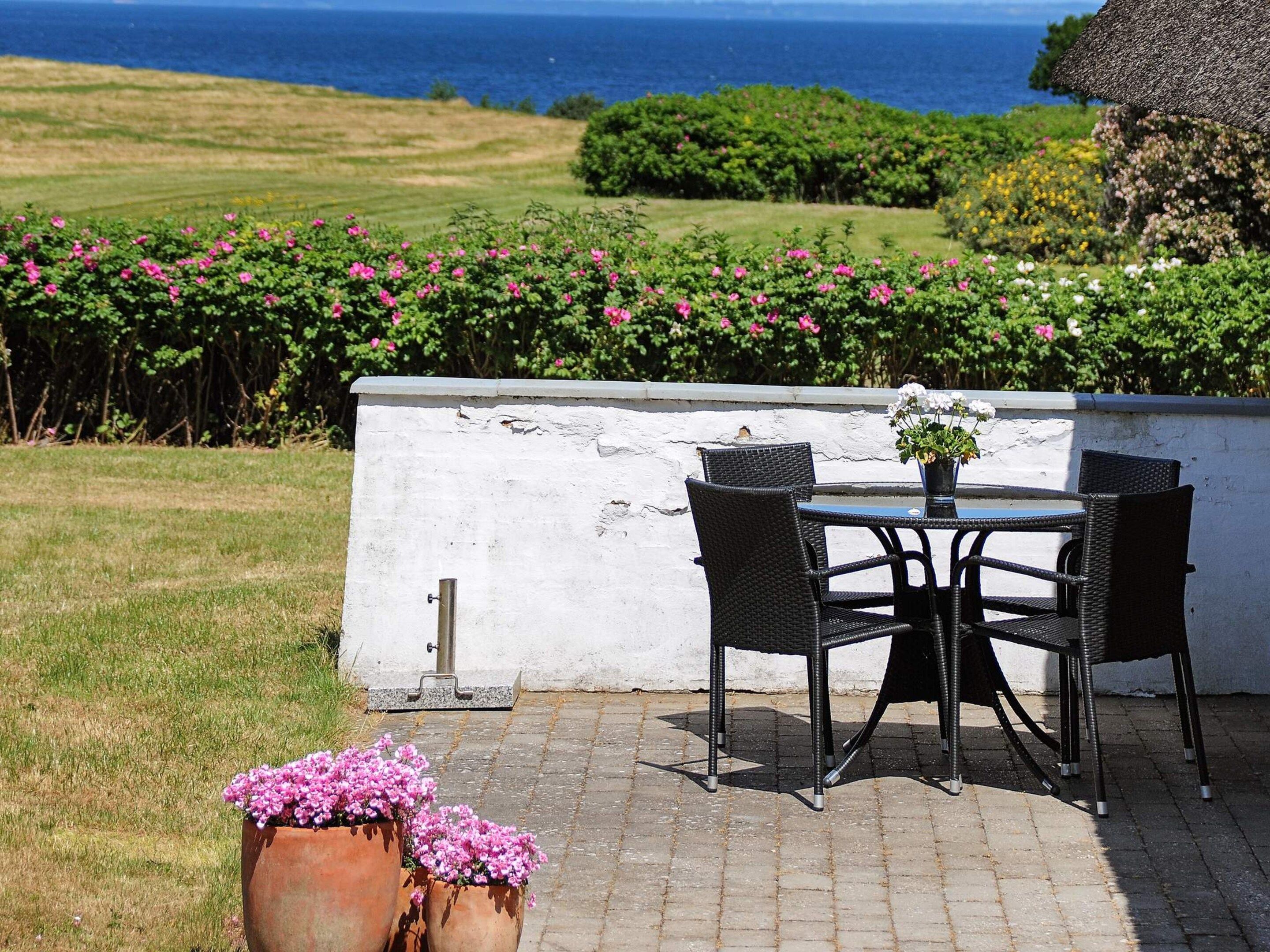 Un espace extérieur aménagé avec une table et des chaises, un mur blanc et une vue sur la mer.