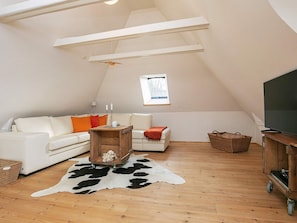 A loft-style living room with a sloped ceiling, a white sofa, a wooden coffee table, a television on a wooden stand, and a cowhide rug. - 4 Star Holiday Home in Asperup (Middelfart)