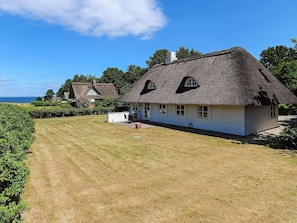 A thatched-roof house with a well-maintained lawn, a small patio, and a view of the sea. - 4 Star Holiday Home in Asperup (Middelfart)