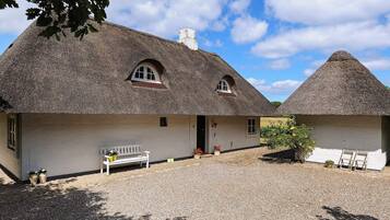 A traditional thatched-roof cottage with a gravel driveway and a bench outside.
