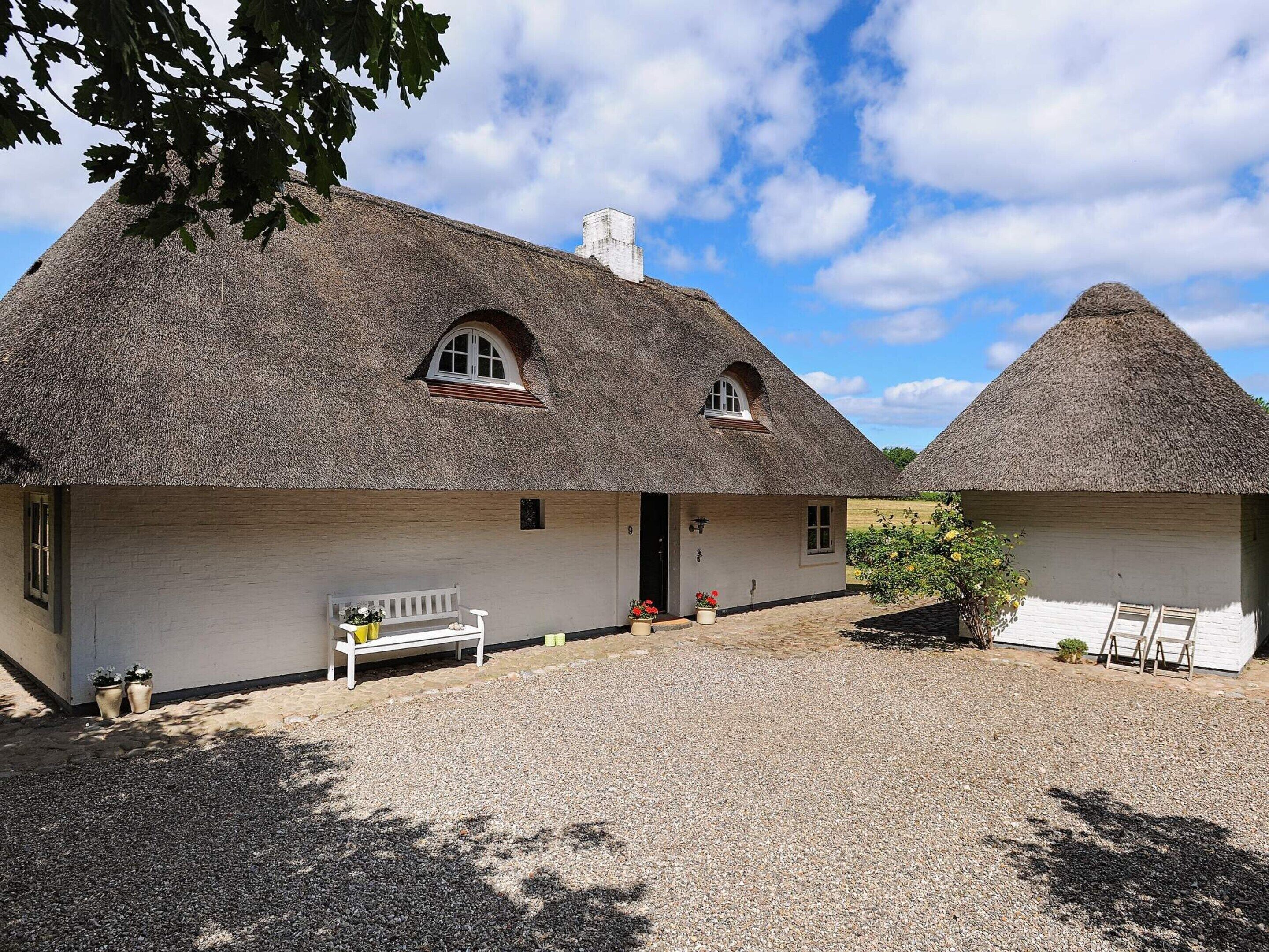 A traditional thatched-roof cottage with a gravel driveway and a bench outside.