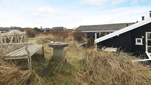 A coastal property with a black house, a wooden bench, and a stone table in a grassy area. - Modern Pool House With View - By Traum Ferienwohnungen (Hjørring)