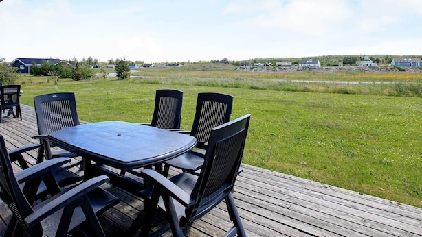 A covered outdoor area with a table and chairs, overlooking a grassy field and distant houses.