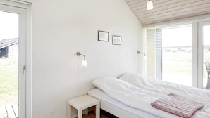 A bedroom with a bed, a small bedside table, a wall-mounted lamp, and a window with a view of the outdoors.