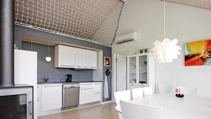 A modern kitchen with white cabinets, a dishwasher, and a stove. There is a dining area with a white table and chairs.
