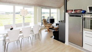A modern kitchen with a built-in stove, a refrigerator, and a dining area with white chairs and a table.
