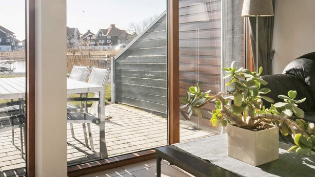 Een kamer met een grote glazen schuifpui die uitkomt op een terras met een tafel en stoelen.