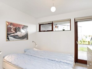 A bedroom with a bed, a wall-mounted lamp, a window with a view, and a framed artwork. - 4 Star Holiday Home in Bogense (Bogense)