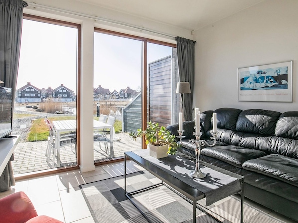 A modern living room with a leather sofa, a coffee table, and a view of a residential area through large windows.