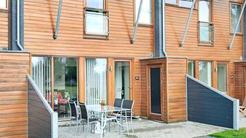 A modern building with a wooden facade, large windows, and a patio area with outdoor seating.